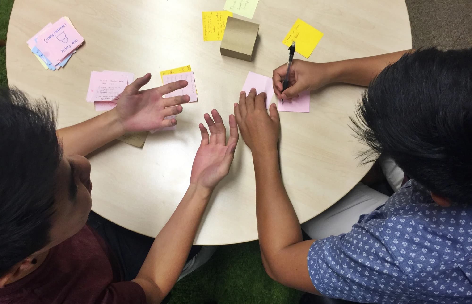 Overhead view of two students’ hands sorting colored post-it notes on a table.
